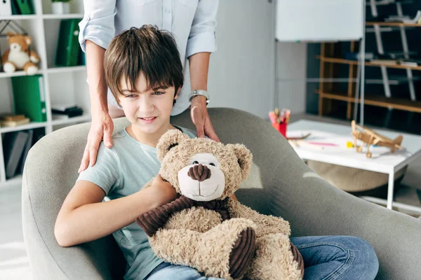 Vista recortada de niño psicólogo abrazo niño con dislexia celebración osito de peluche - foto de stock