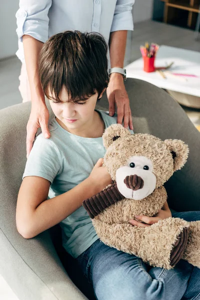 Vista recortada de niño psicólogo abrazo niño con dislexia celebración osito de peluche - foto de stock