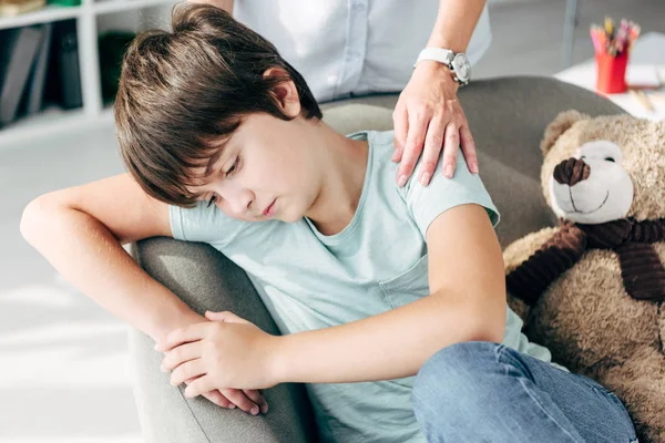 Vista recortada de psicólogo infantil abrazando a niño triste con dislexia - foto de stock