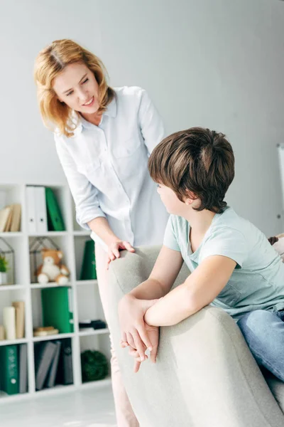Kid with dyslexia sitting on armchair and talking with child psychologist — Stock Photo