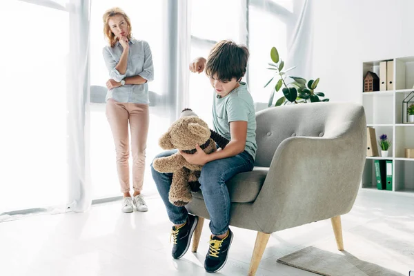 Enfant en colère avec dyslexie poinçonnage ours en peluche et psychologue enfant en regardant — Photo de stock