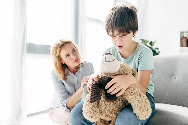 Enfant irrité avec dyslexie tenant ours en peluche et psychologue enfant le regardant — Photo de stock