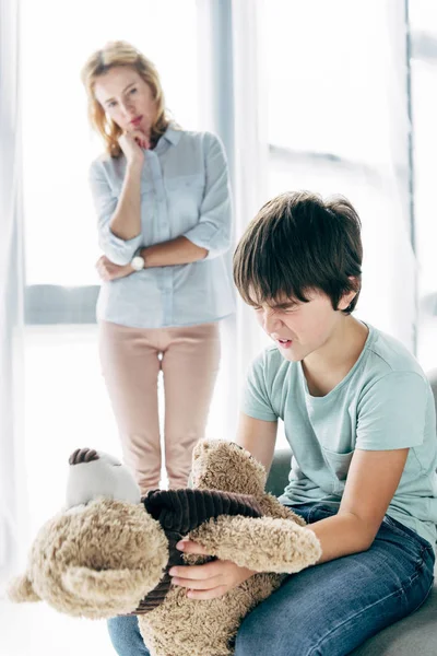 Bambino triste con dislessia con orsacchiotto in mano e psicologo infantile che lo guarda — Foto stock