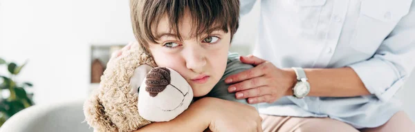 Plano panorámico de niño con dislexia sosteniendo osito de peluche y psicólogo infantil abrazándolo - foto de stock