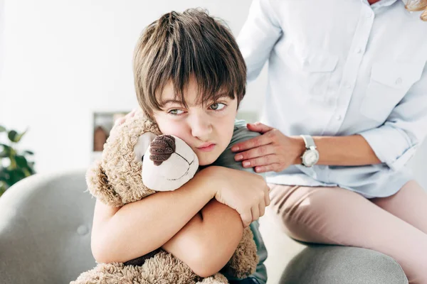 Sad kid with dyslexia holding teddy bear and child psychologist hugging him — Stock Photo