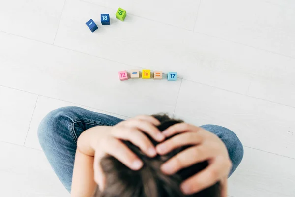 Vue de dessus de l'enfant triste avec dyslexie assis près des blocs de construction — Photo de stock