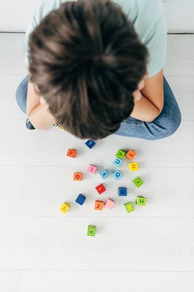 Vue de dessus de l'enfant triste avec dyslexie assis près des blocs de construction — Photo de stock