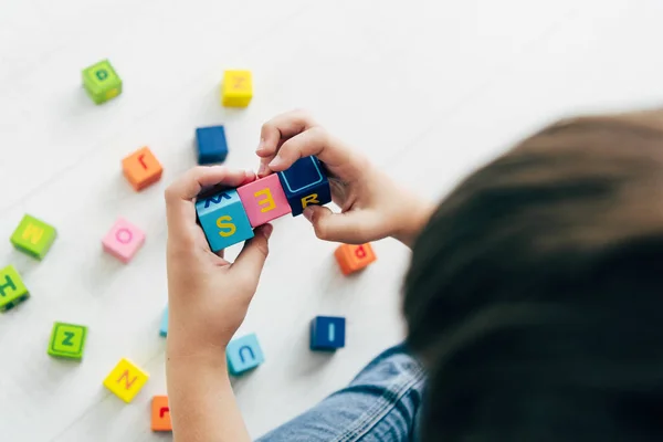 Vue recadrée de l'enfant avec dyslexie jouer avec des blocs de construction colorés — Photo de stock