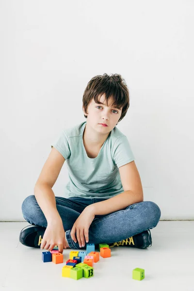 Kid with dyslexia sitting on floor with building blocks on white background — Stock Photo