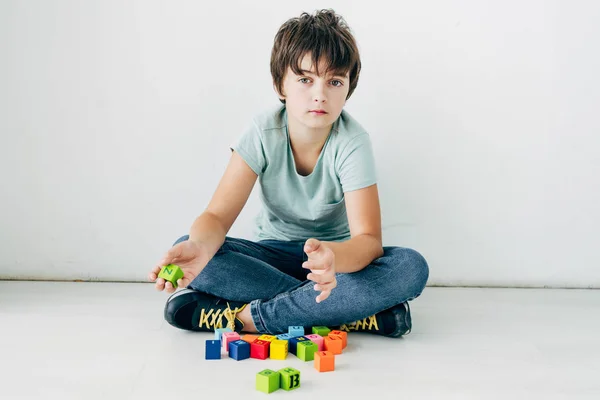 Kid with dyslexia sitting on floor with building blocks on white background — Stock Photo