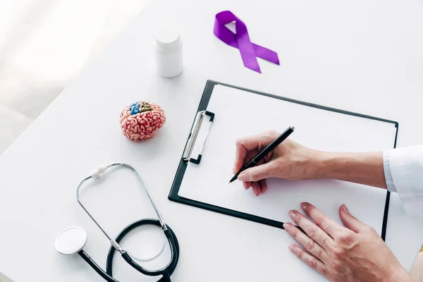 Vista recortada del médico escribiendo en el portapapeles con pluma - foto de stock