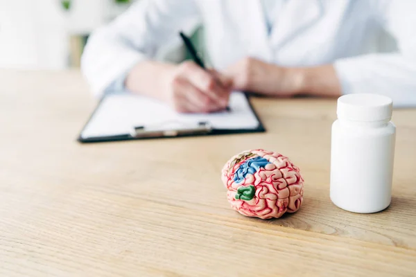Selective focus of bottle with pills and model of brain on wooden table — Stock Photo