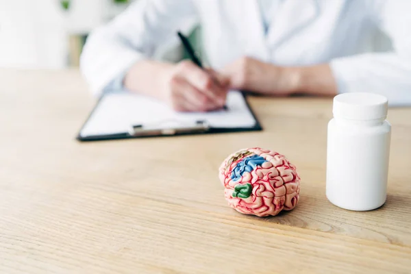 Enfoque selectivo de la botella con pastillas y el modelo de cerebro en la mesa de madera - foto de stock