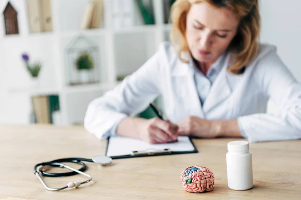 Selective focus of bottle with pills, stethoscope and model of brain on wooden table — Stock Photo