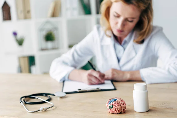 Foyer sélectif de la bouteille avec des pilules, stéthoscope et modèle de cerveau sur table en bois — Photo de stock