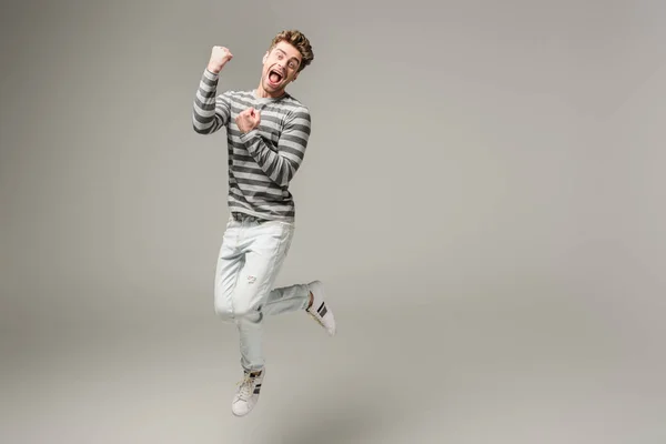 Excited screaming man jumping and cheering on grey — Stock Photo