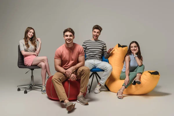 Happy friends sitting on different chairs, on grey — Stock Photo