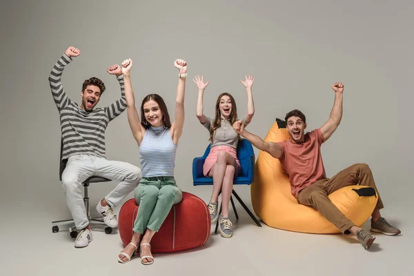 Amigos animadores emocionais sentados em cadeiras diferentes, em cinza — Fotografia de Stock