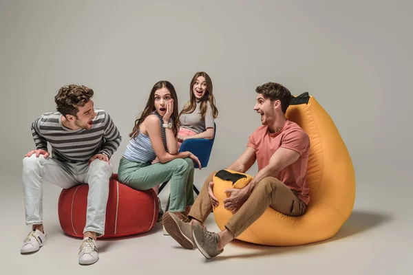 Schockierte Freunde sitzen auf verschiedenen Stühlen, auf grauen — Stockfoto
