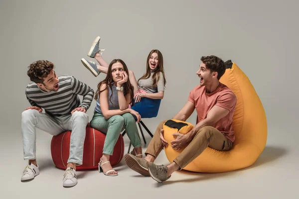 Emotional friends sitting on different chairs, on grey — Stock Photo