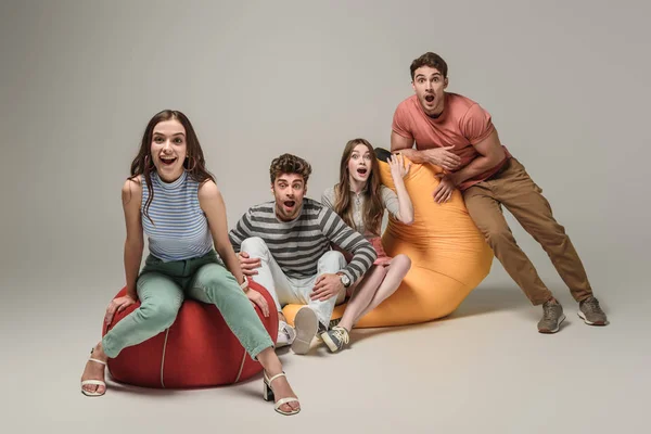 Surprised friends sitting on bin bag chairs together, on grey — Stock Photo