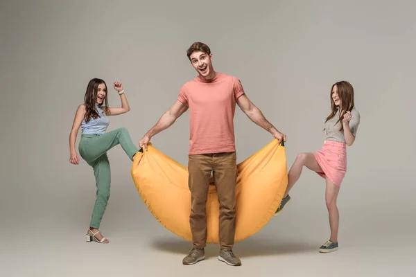 Friends having fun with bin bag chair together, on grey — Stock Photo