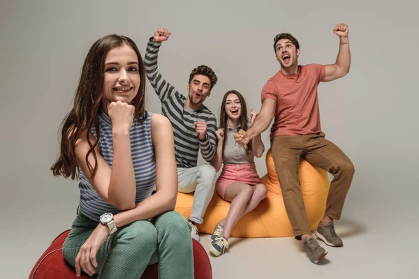 Cheering friends sitting on bin bag chairs together, on grey — Stock Photo