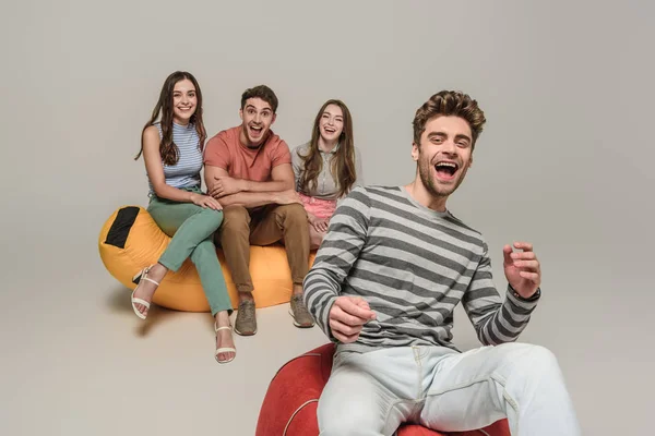 Amis excités assis sur des chaises de sac poubelle ensemble, sur gris — Photo de stock