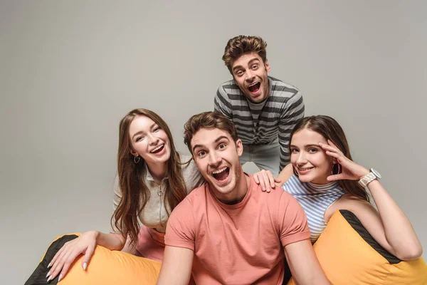 Excited friends sitting on bin bag chair together, isolated on grey — Stock Photo