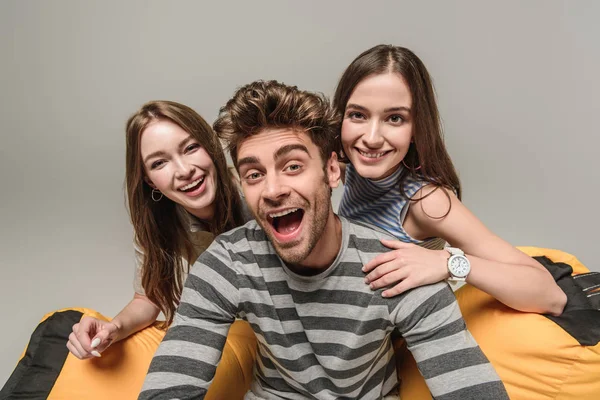 Amis excités assis sur une chaise poubelle ensemble, isolé sur gris — Photo de stock