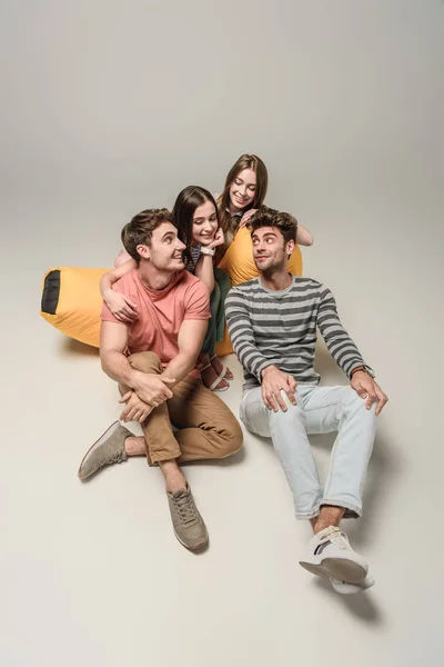 Amigos felices sentados en la silla de la bolsa de basura juntos, en gris - foto de stock