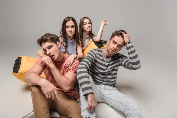 Amis sérieux assis sur une chaise poubelle ensemble, sur gris — Photo de stock