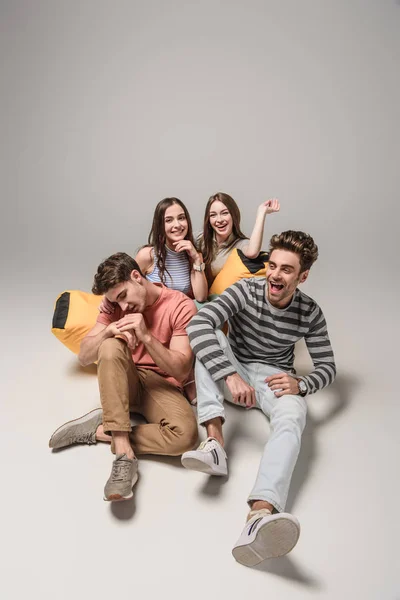 Laughing friends sitting on bin bag chair together, on grey — Stock Photo