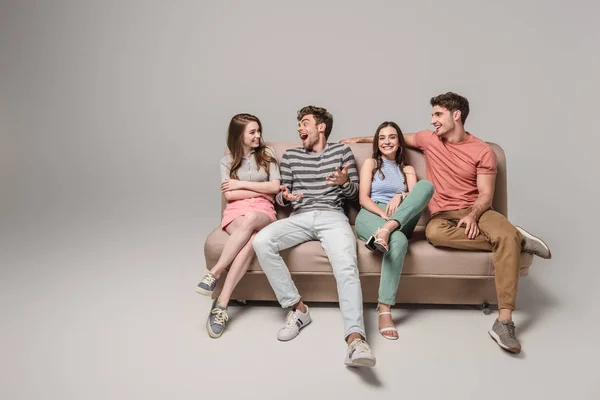 Щасливі молоді друзі розмовляють і сидять на дивані на сірому — стокове фото