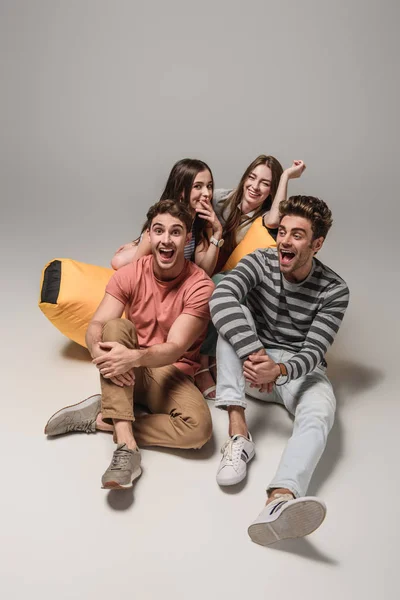 Amigos riendo sentados en la silla de la bolsa de basura juntos, en gris - foto de stock