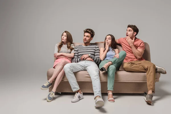 Schockierte junge Freunde sitzen zusammen auf Sofa in Grau — Stockfoto