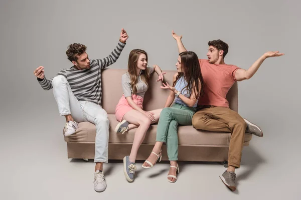 Emotionale junge Freunde reden und sitzen auf dem Sofa auf grau — Stockfoto