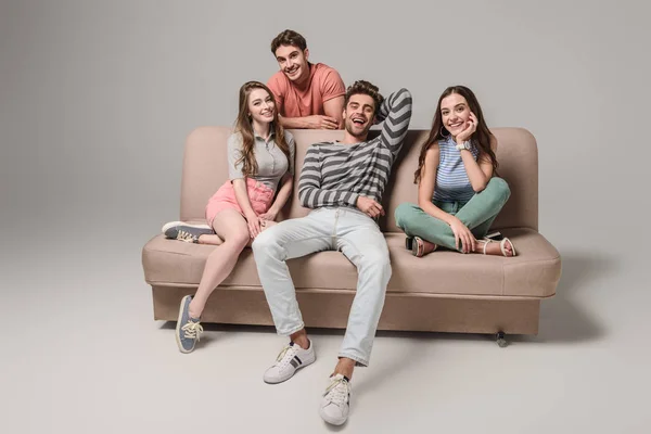 Усміхнені молоді друзі сидять на дивані на сірому — стокове фото