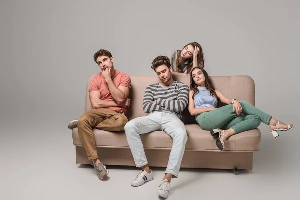 Нудні і стомлені друзі сидять разом на дивані на сірому — стокове фото