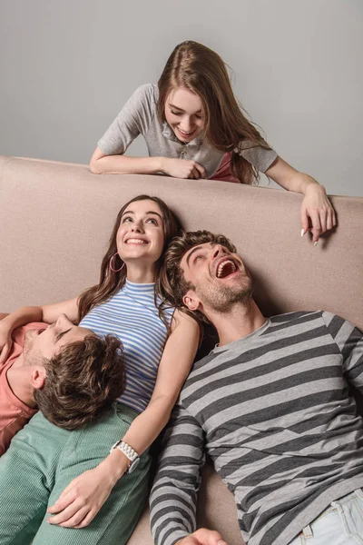 Happy young friends resting together on sofa isolated on grey — Stock Photo