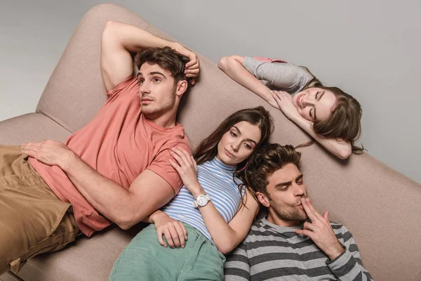 Bored sad friends lying together on sofa isolated on grey — Stock Photo