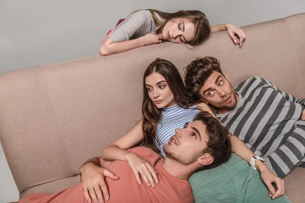 Скучающие молодые друзья, лежащие вместе на диване, изолированном от серых — стоковое фото