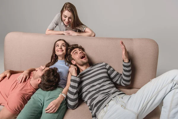 Happy young friends resting on sofa isolated on grey — Stock Photo