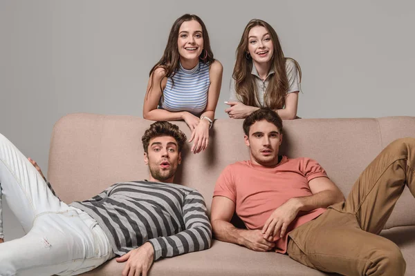 Jovens amigos felizes sentados no sofá isolado no cinza — Fotografia de Stock