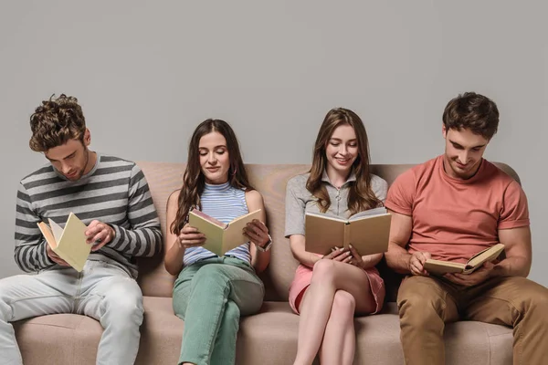 Junge Freunde lesen Bücher, während sie auf dem Sofa auf grau sitzen — Stockfoto