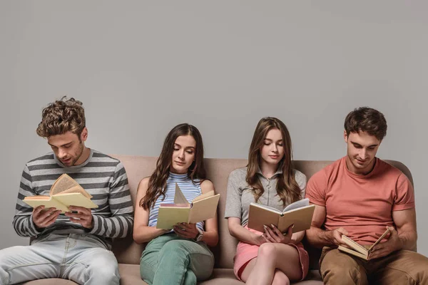 Jóvenes amigos aburridos leyendo libros mientras están sentados en el sofá en gris - foto de stock