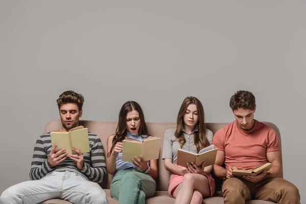 Amigos aburridos leyendo libros mientras están sentados en el sofá en gris — Stock Photo