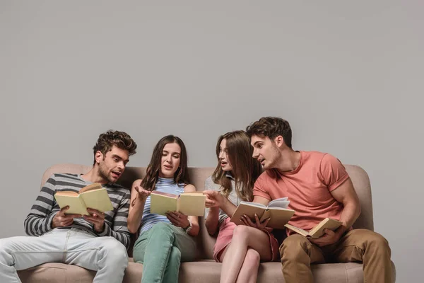 Amigos falando e lendo livros enquanto sentado no sofá em cinza — Fotografia de Stock