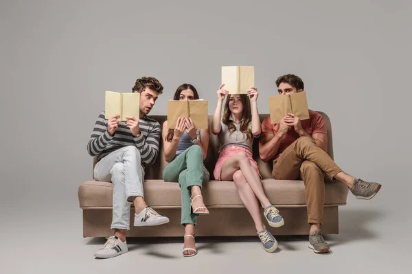 Shocked friends reading books while sitting on sofa on grey — Stock Photo