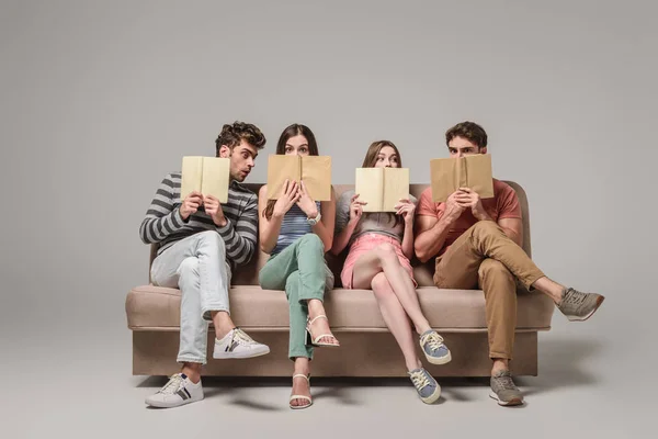 Friends holding books while sitting on sofa on grey — Stock Photo